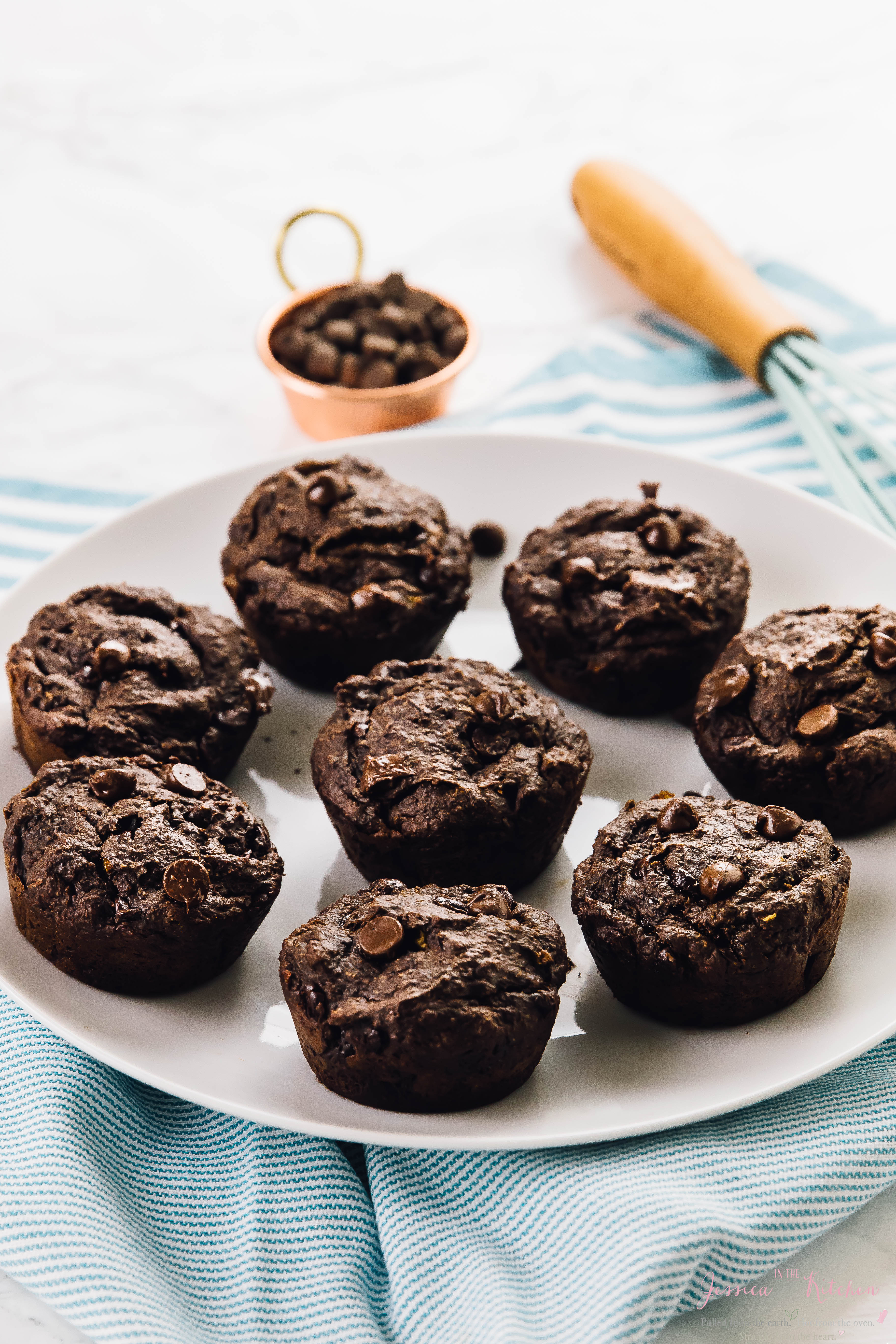 A plate full of chocolate banana muffins with a whisk in the background.