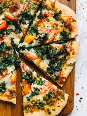 Top down shot of kale pesto pizza slices on a board.