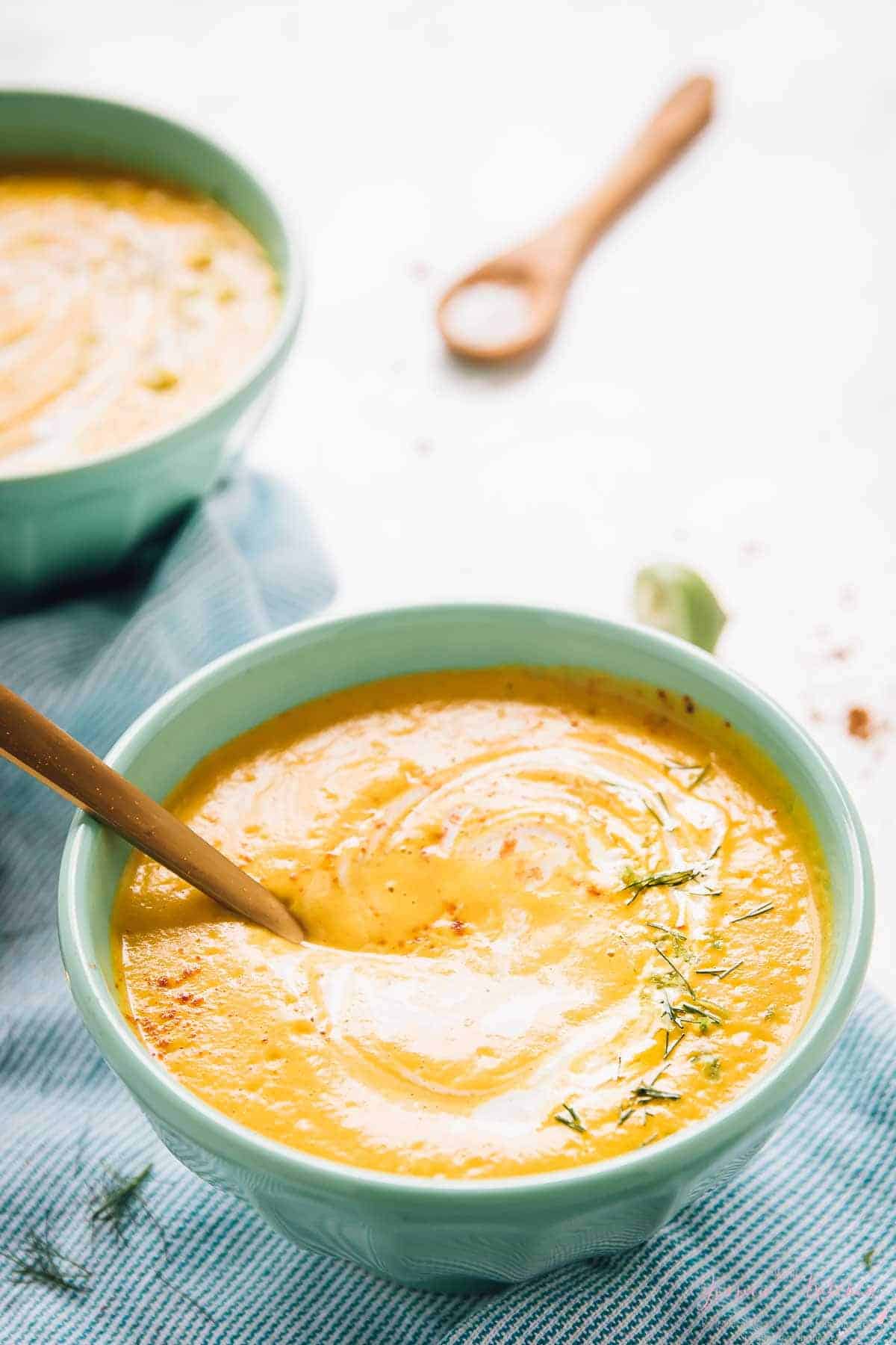 Roasted carrot soup in a blue bowl, with a spoon dipped in it. 