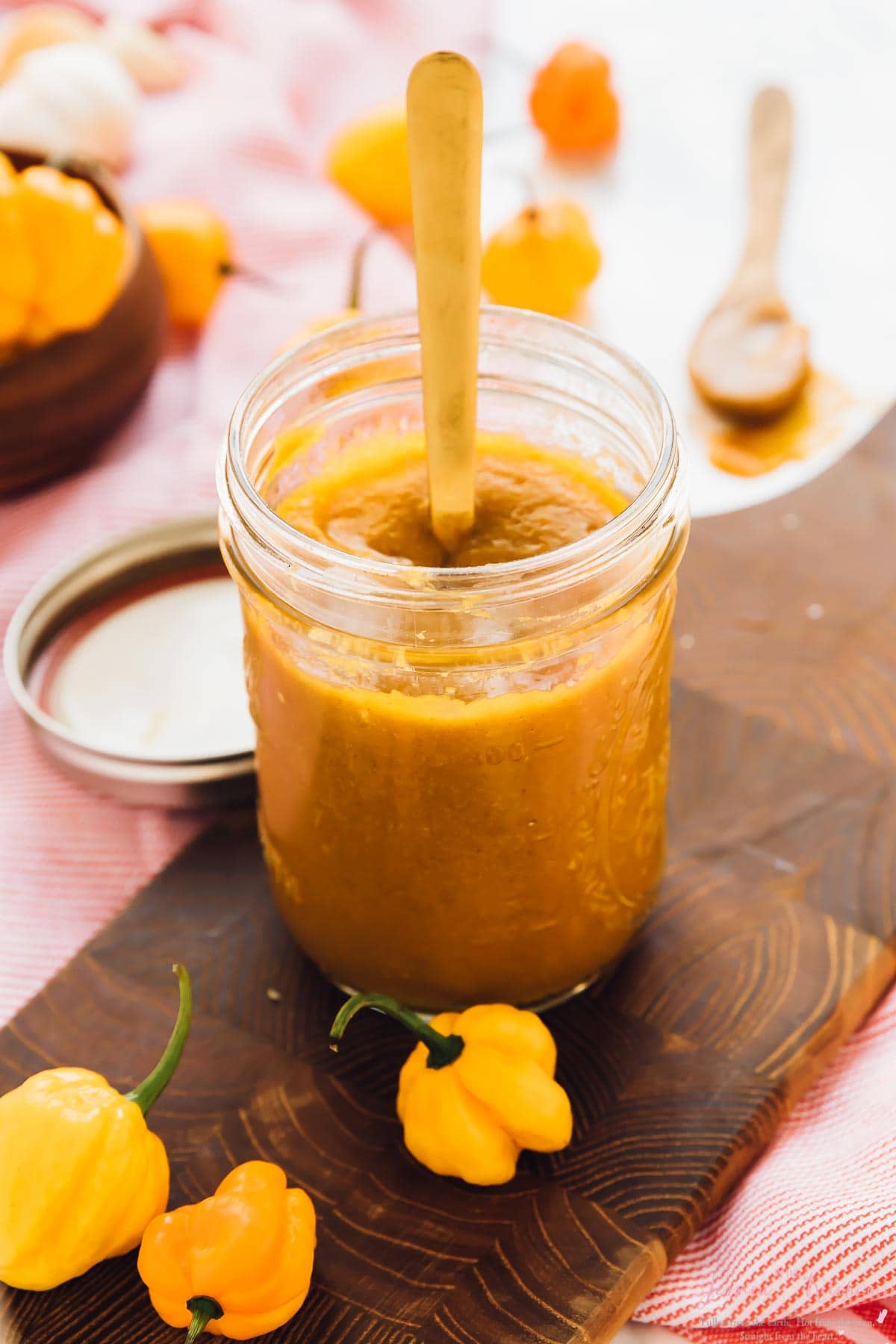 A glass jar containing scotch bonnet pepper hot sauce with peppers on the side. 