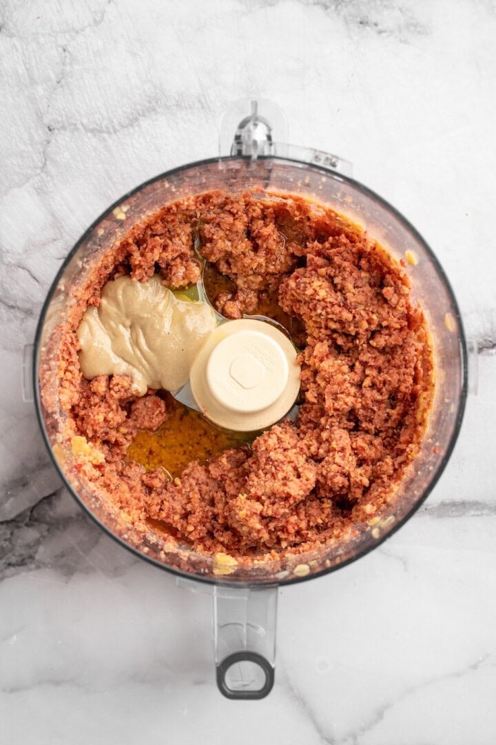 Overhead view of tahini added to food processor with pulsed beets and chickpeas
