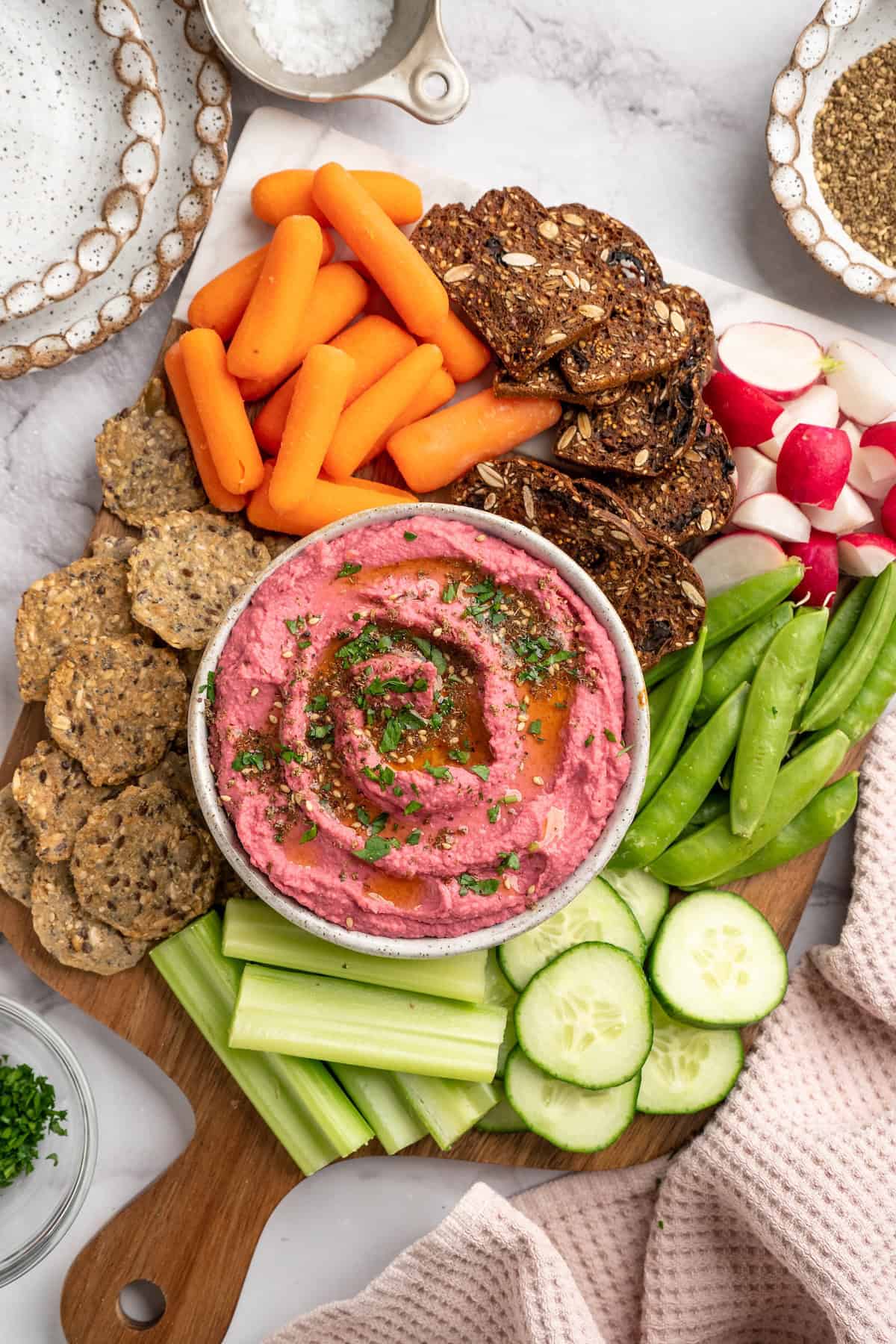 Wooden board with bowl of beet hummus, crackers, and raw vegetables