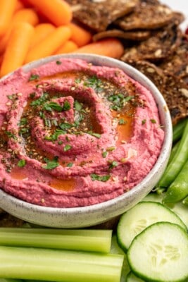 Beet hummus in bowl surrounded by crudite and crackers