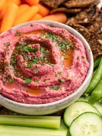 Beet hummus in bowl surrounded by crudite and crackers