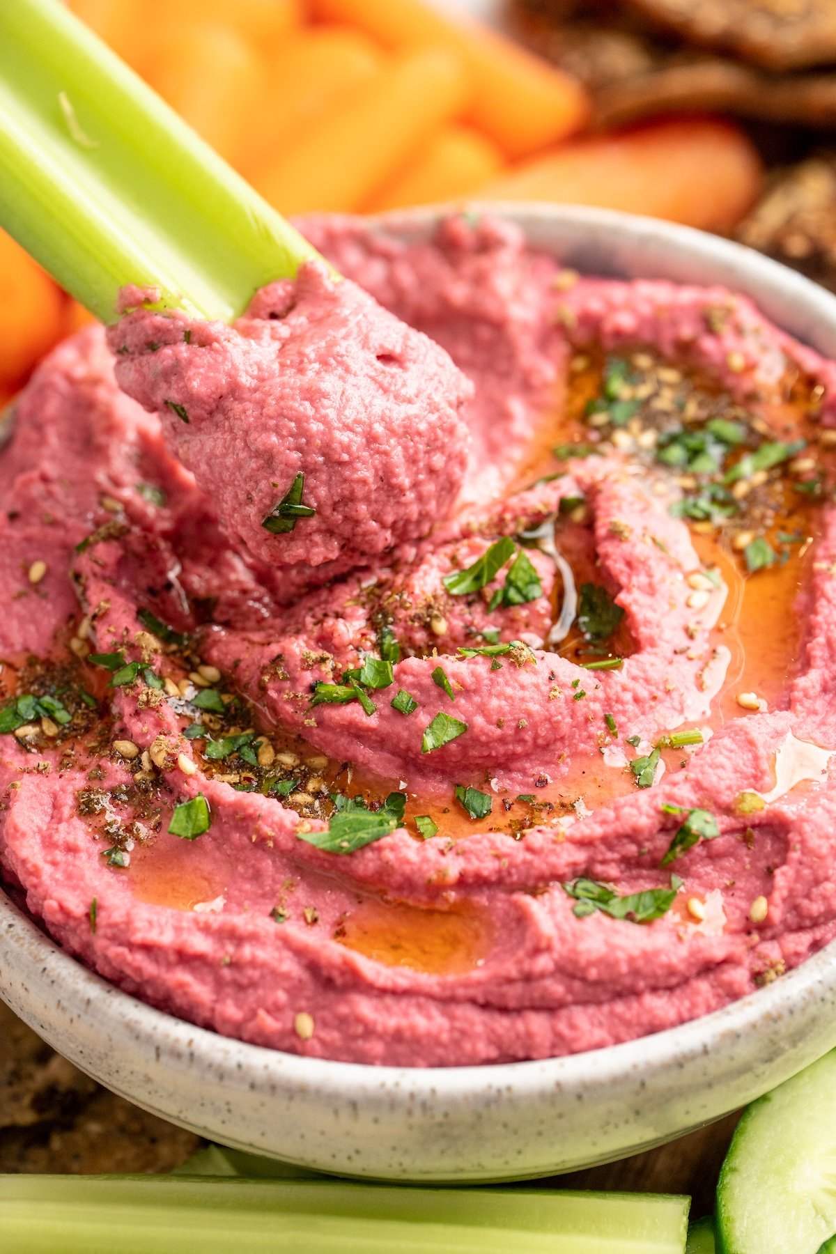Celery scooping beet hummus from bowl