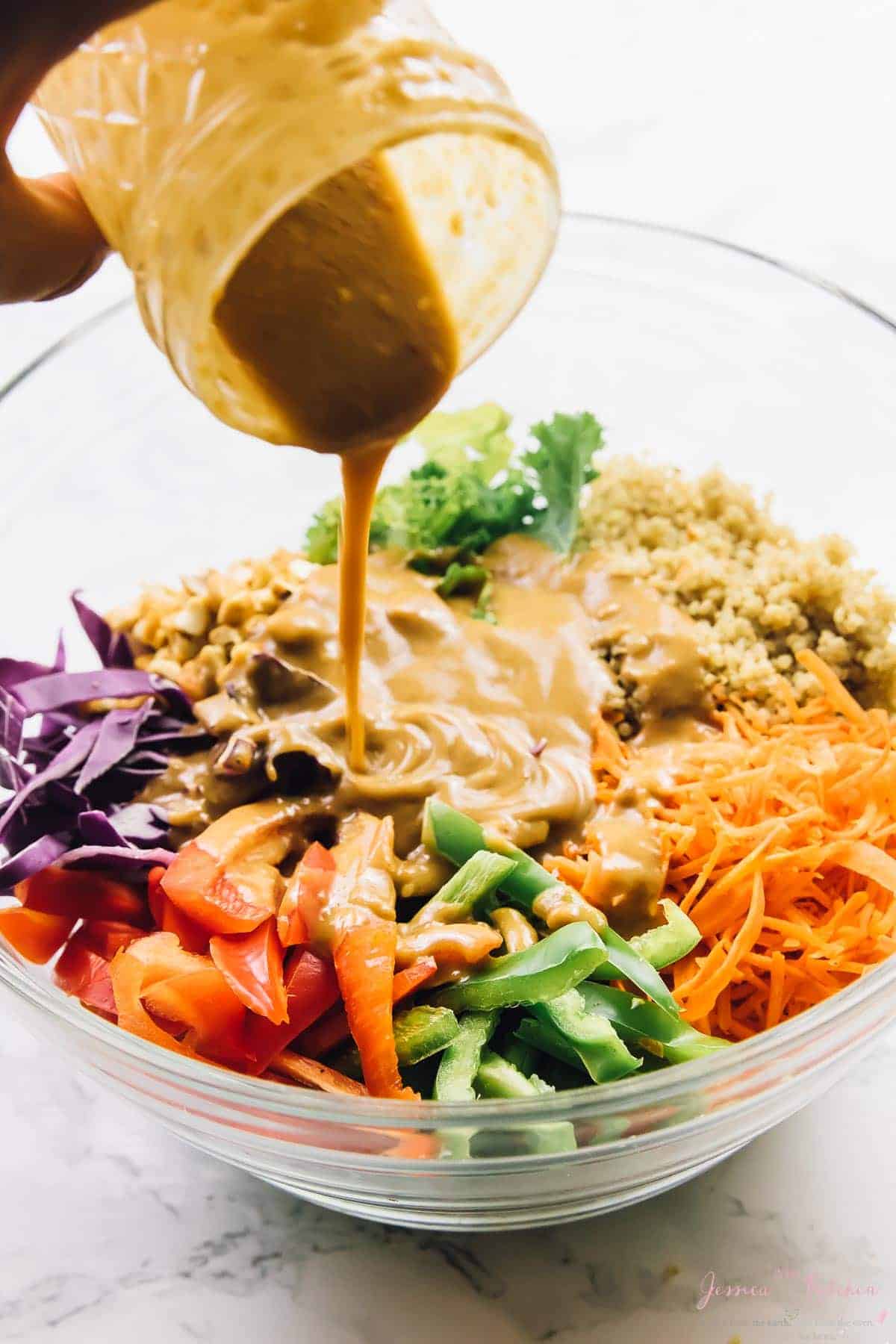 Peanut ginger sauce being poured onto thai quinoa salad in a glass bowl. 