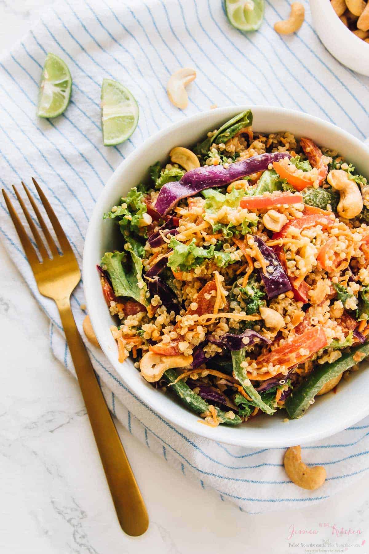 Top down view of cashew thai quinoa salad in a white bowl, with a gold fork on the side. 