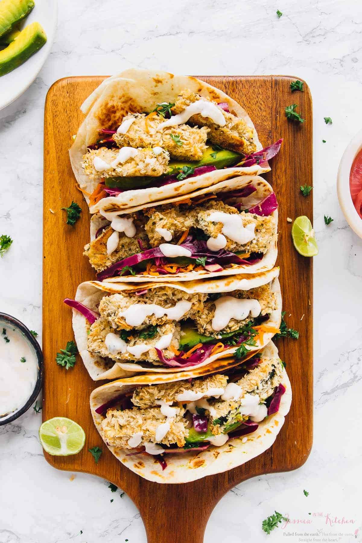 Crispy zucchini tacos on a wood board with cream in a bowl on the side.