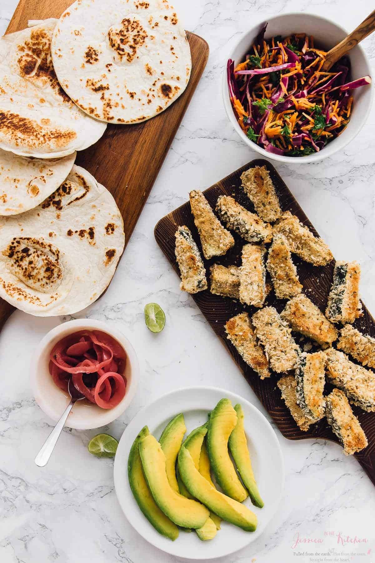 Overhead view of components for crispy zucchini tacos, including zucchini, slaw, avocado, and tortillas