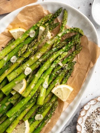Serving plate with garlic roasted asparagus and lemon wedges.