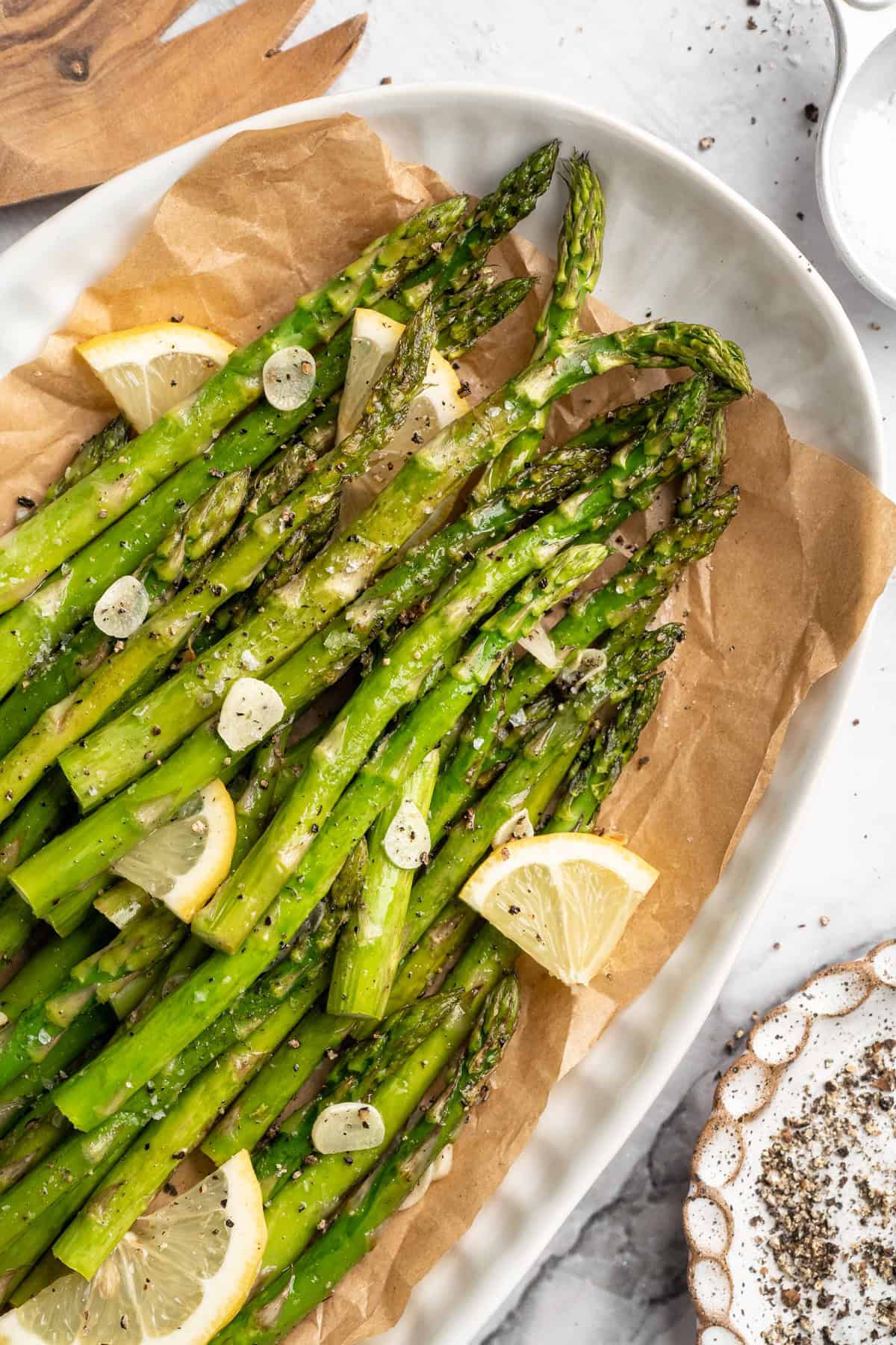 Serving plate with garlic roasted asparagus and lemon wedges.