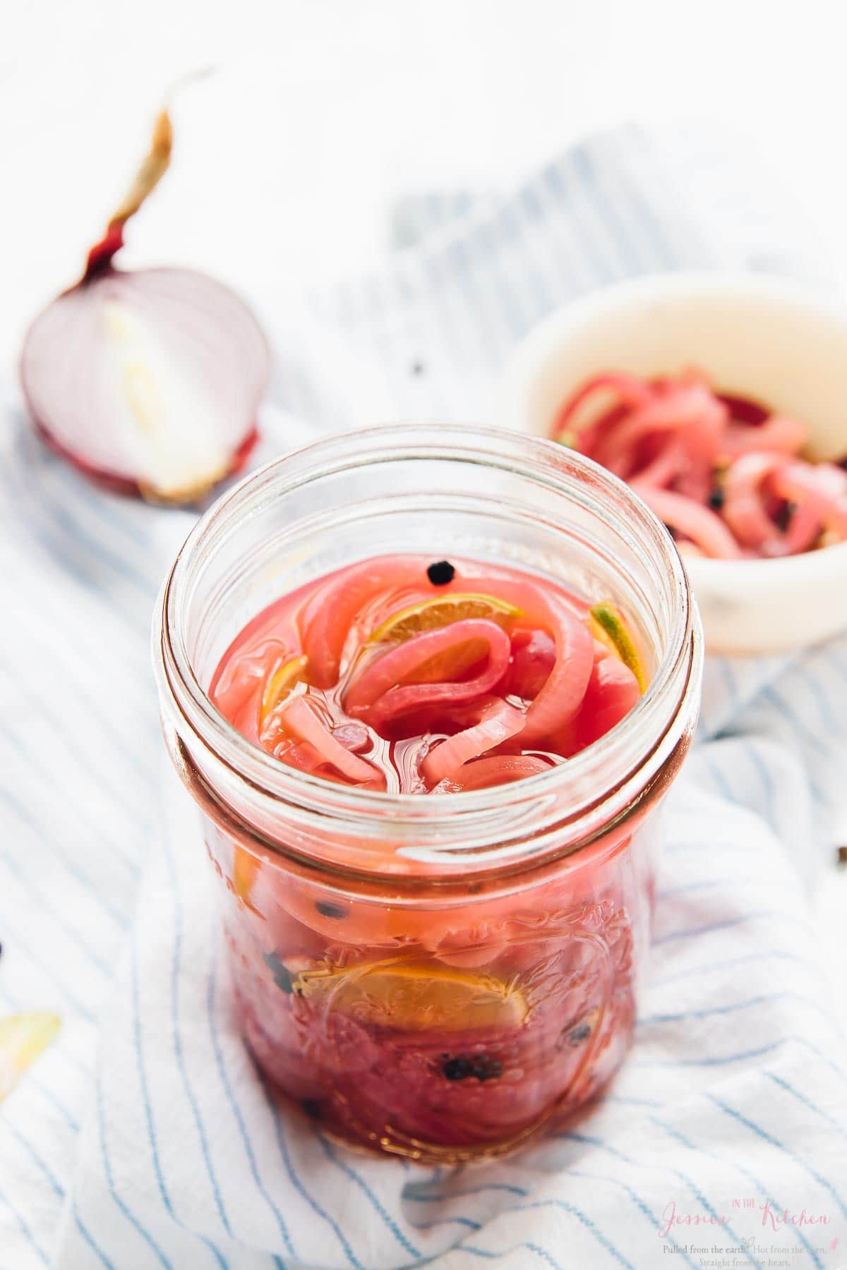 A jar of quick pickled onions with half an onion in the background.