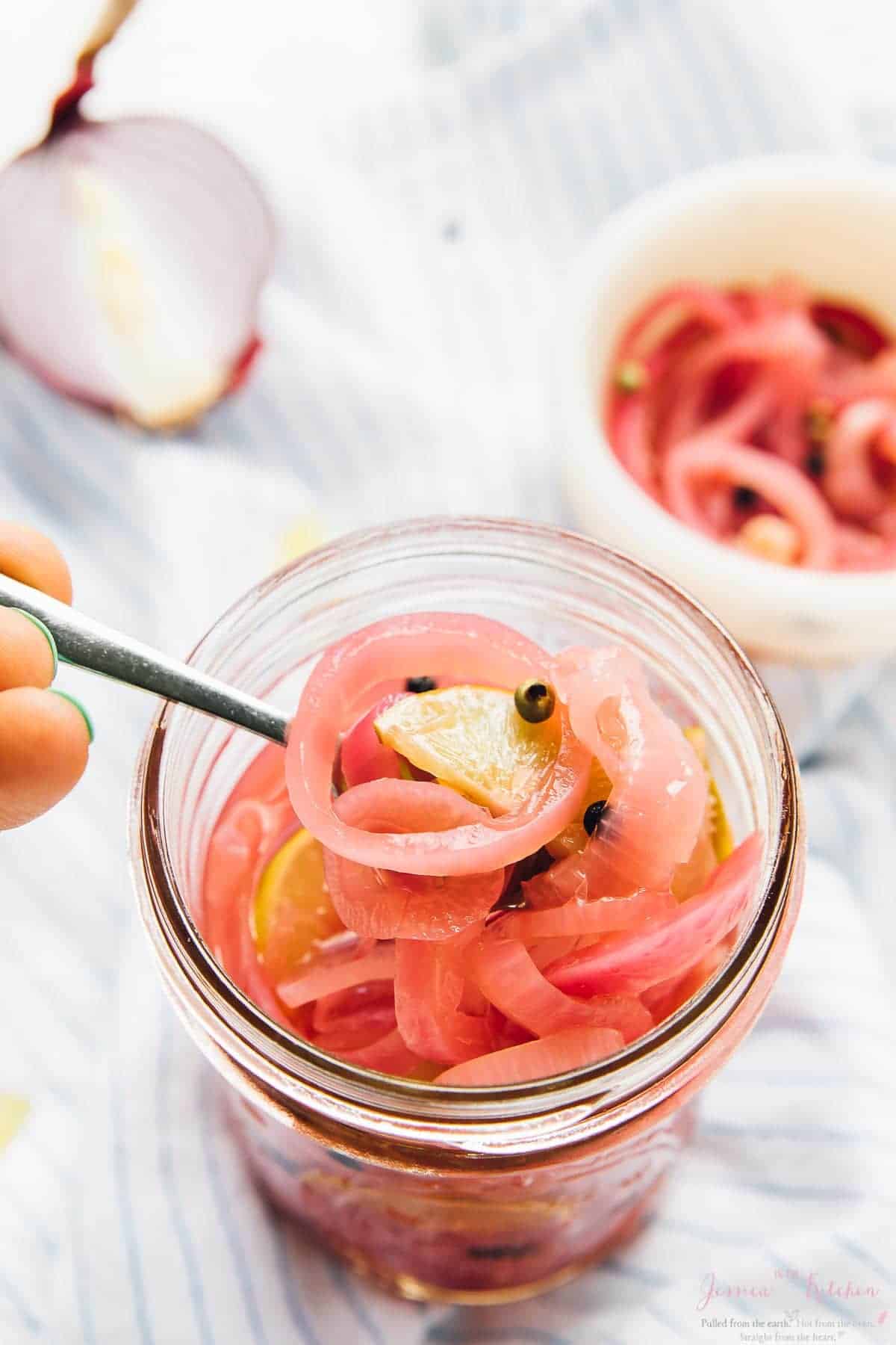 A small spoon scooping out some pickled onions from a glass jar. 