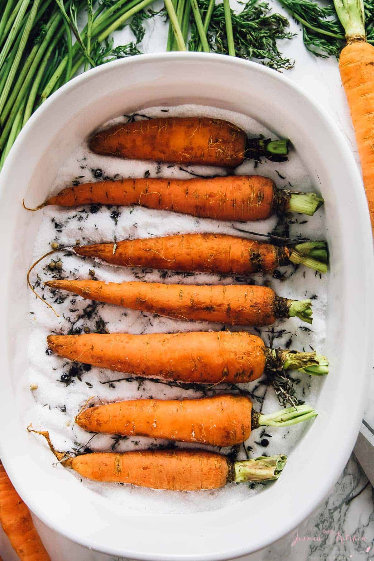 Carrots in a white baking dish on a bed of salt .