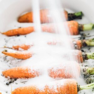 Some carrots being covered with salt in a baking dish.