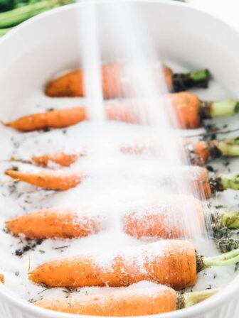 Some carrots being covered with salt in a baking dish.