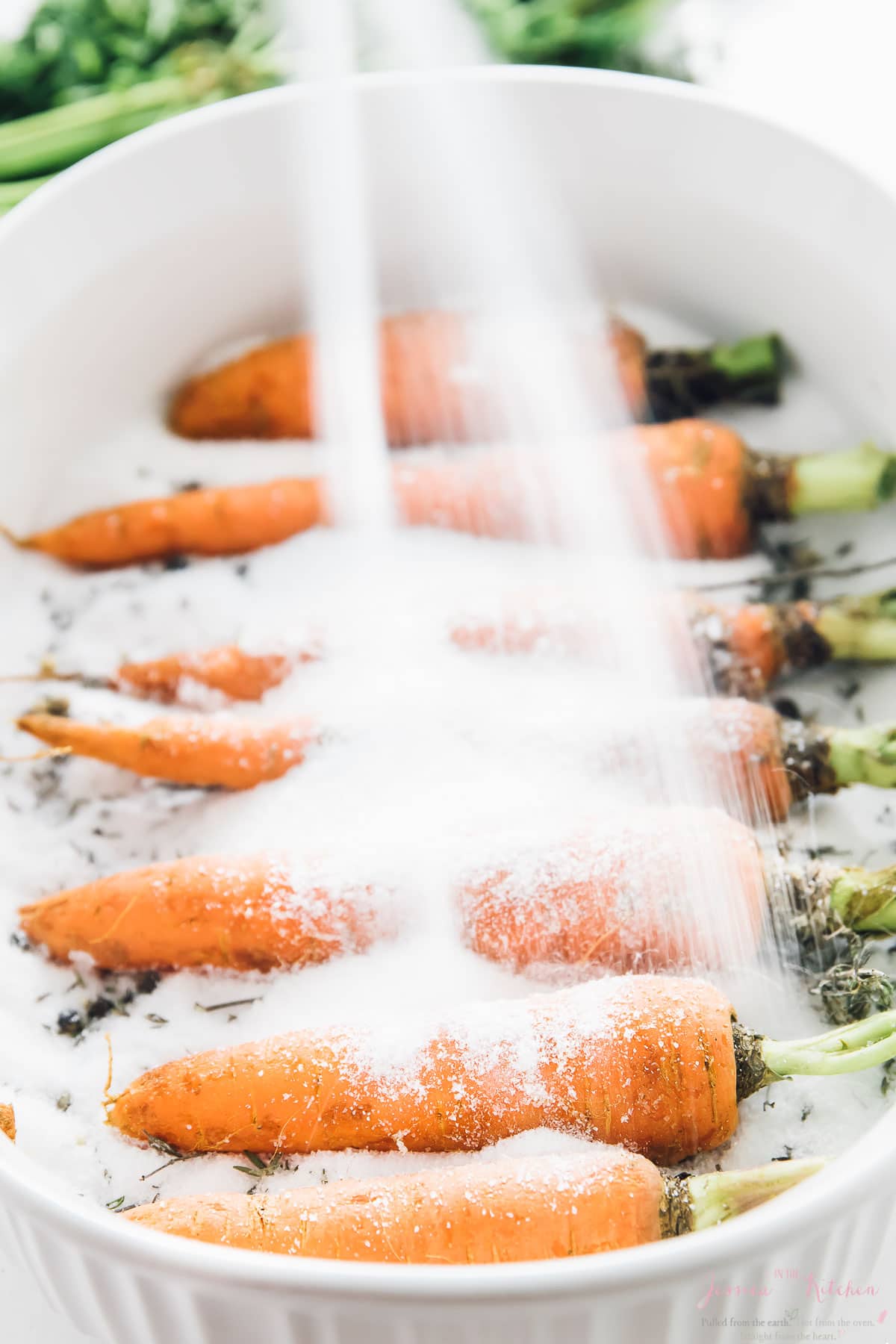 Pouring salt on carrots in a baking dish.