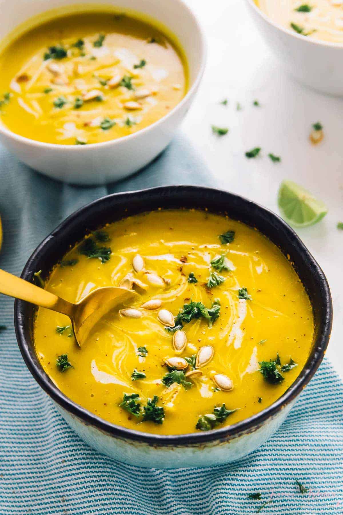 A gold spoon dipping into a black bowl of butternut squash soup.