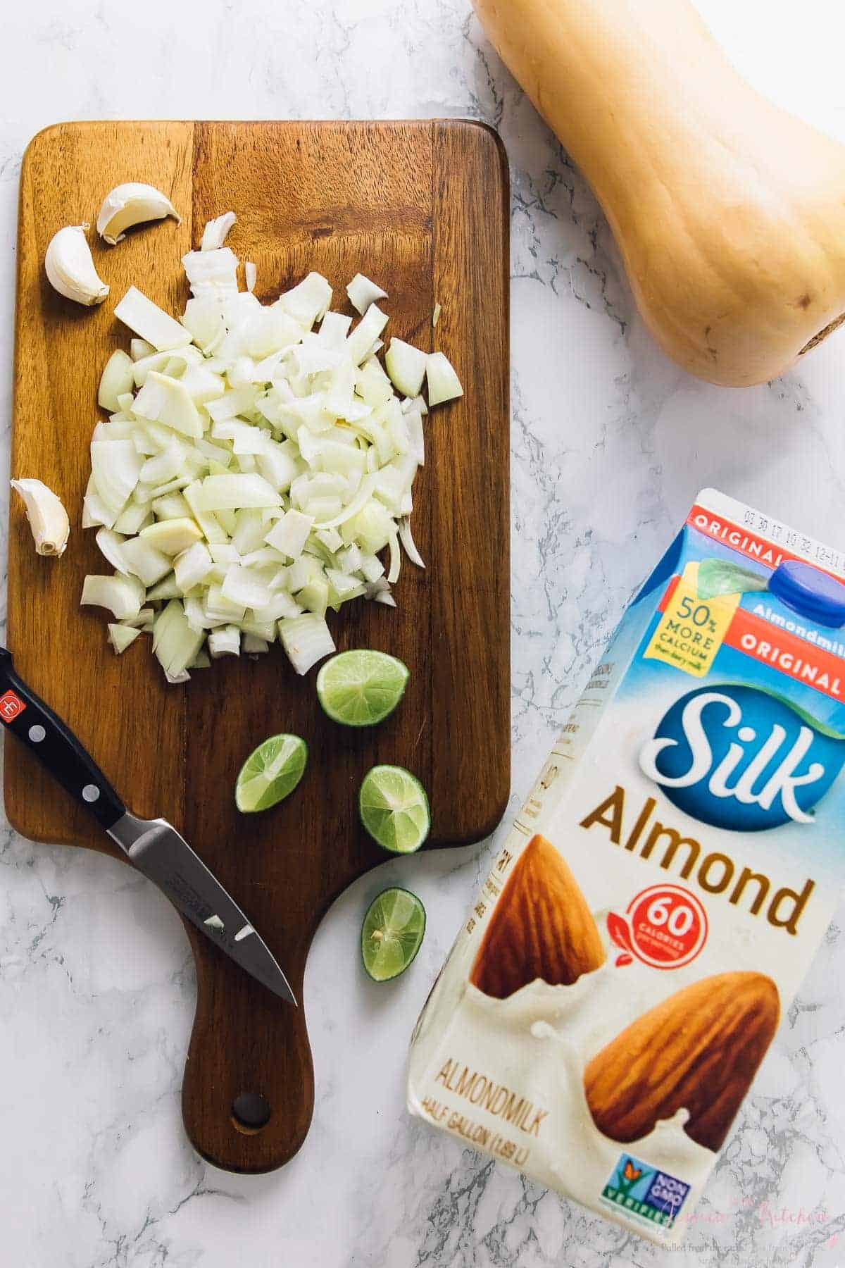 Top down shot of diced onions, lime wedges, butternut squash and a carton of almond milk. 