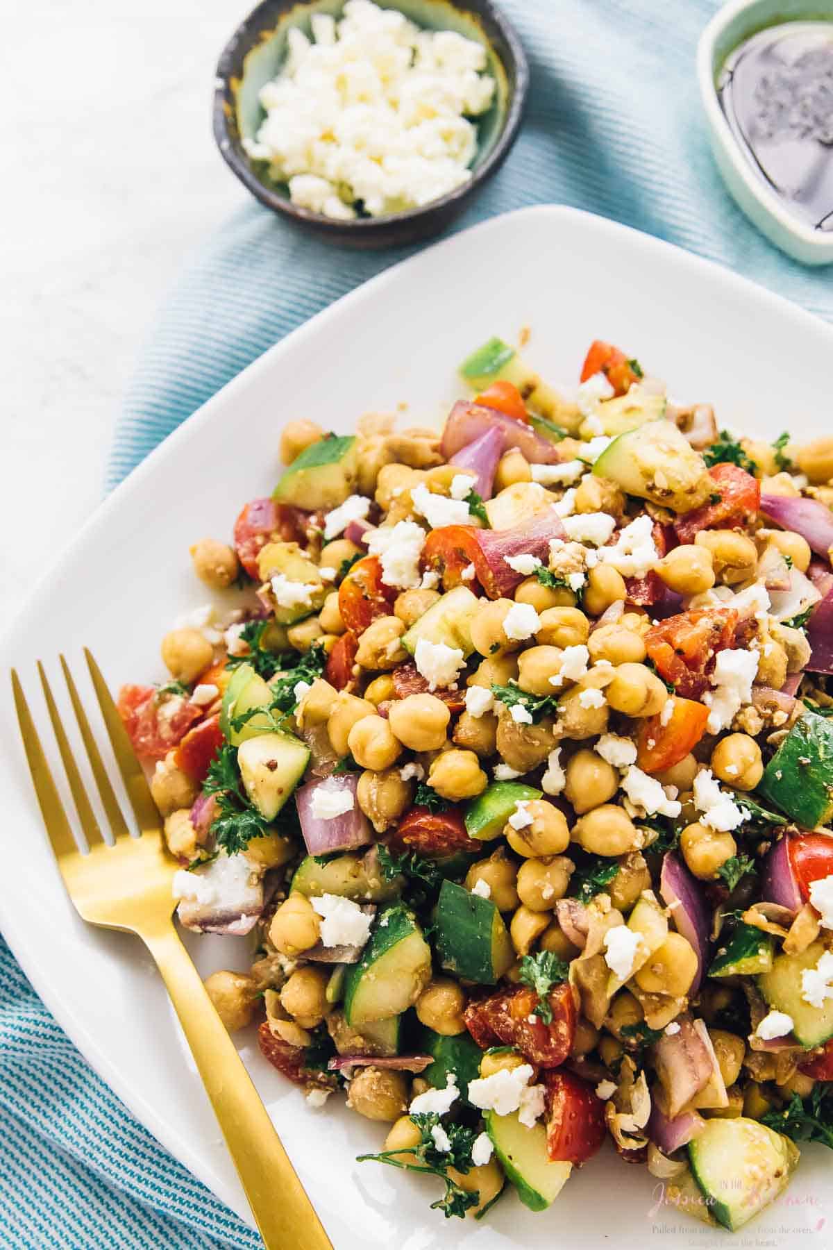 Mediterranean chickpea salad on a square plate with a gold fork.