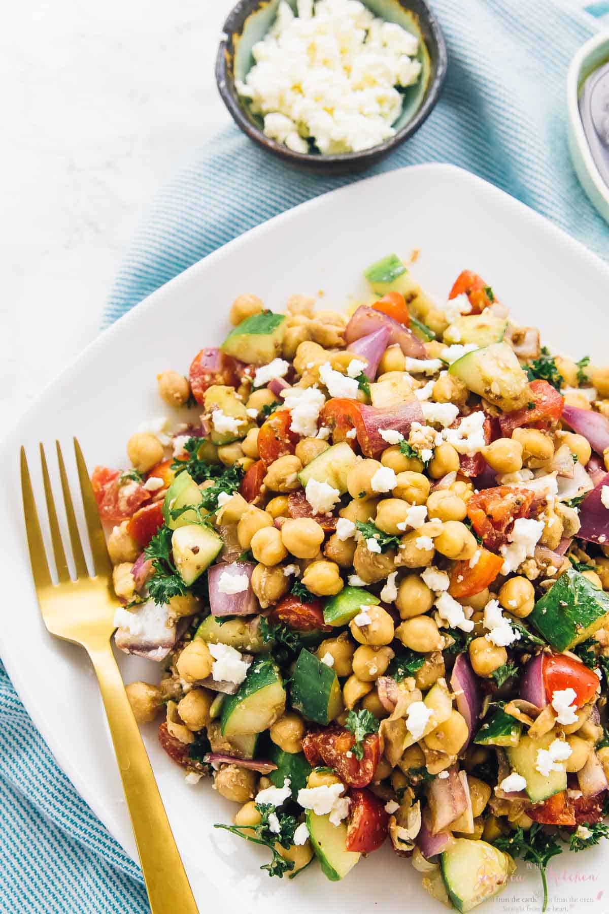 Mediterranean chickpea salad on a white plate with a gold fork on the side. 