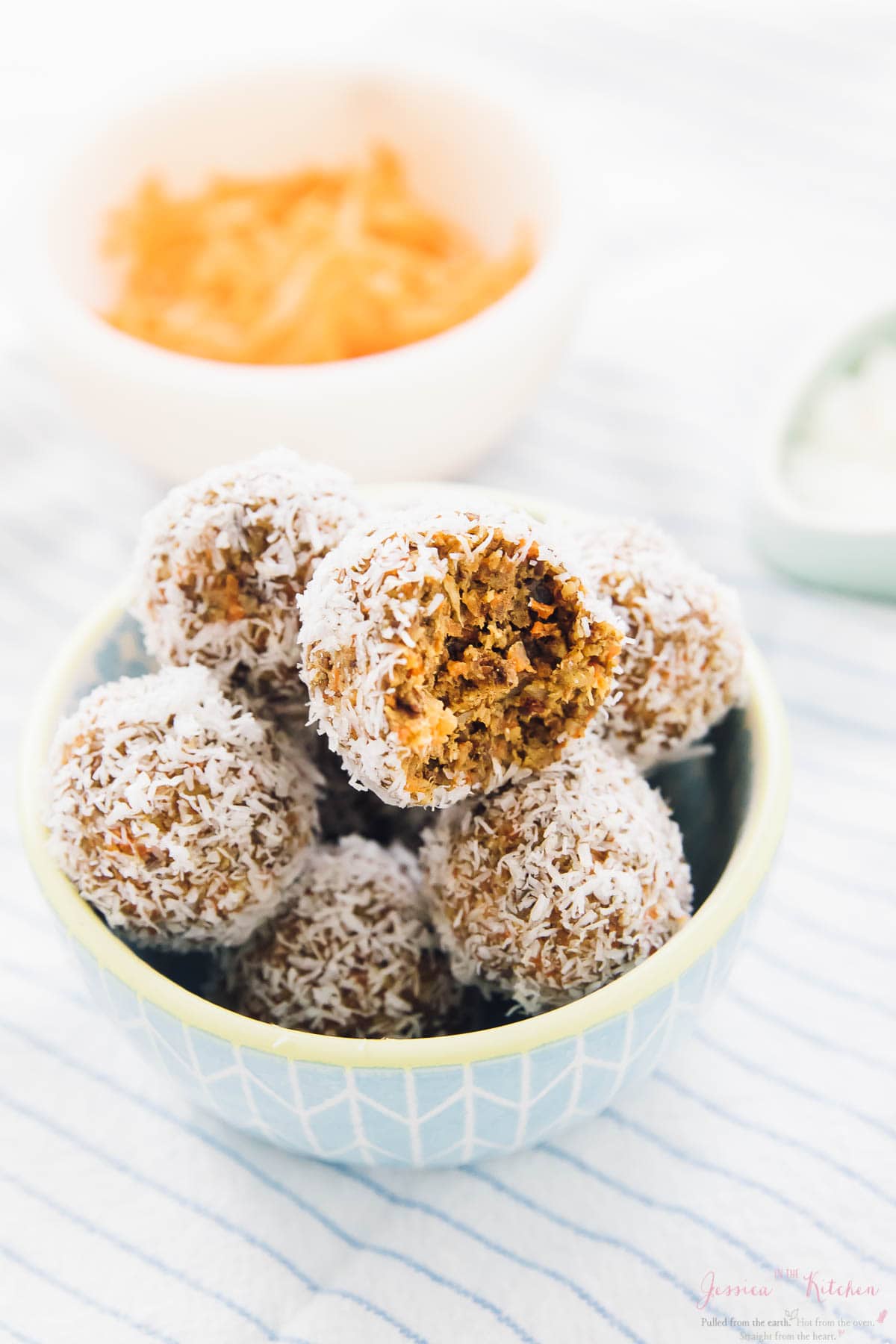 Carrot cake energy bites in a blue bowl with a bowl of shredded carrots in the background. 