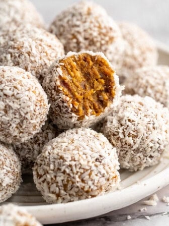 Plate of no bake carrot cake energy bites with one bitten into to show inside.