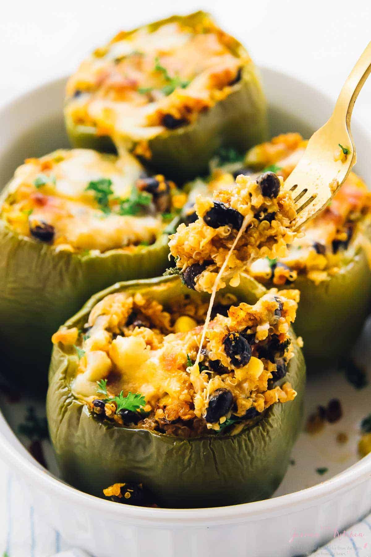 Four quinoa stuffed peppers in a white baking dish. 