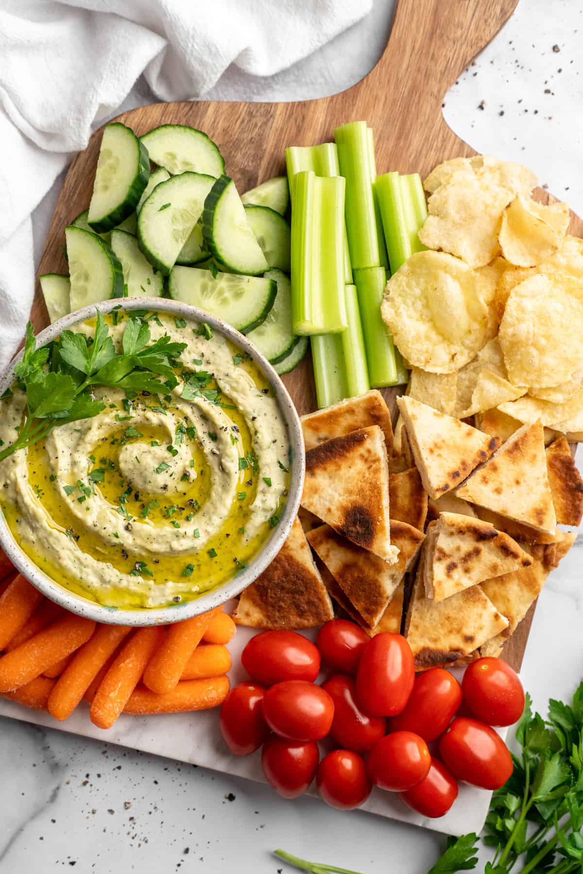 Board with fresh vegetables, potato chips, pita chips, and roasted garlic white bean dip.