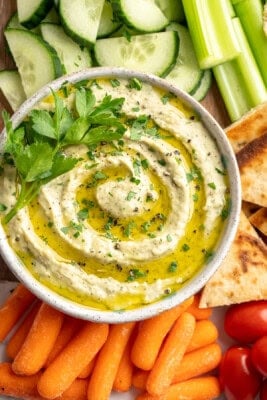 Bowl of roasted garlic white bean dip with fresh vegetables and pita chips.