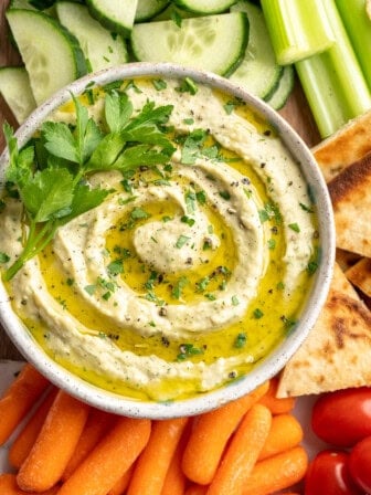 Bowl of roasted garlic white bean dip with fresh vegetables and pita chips.