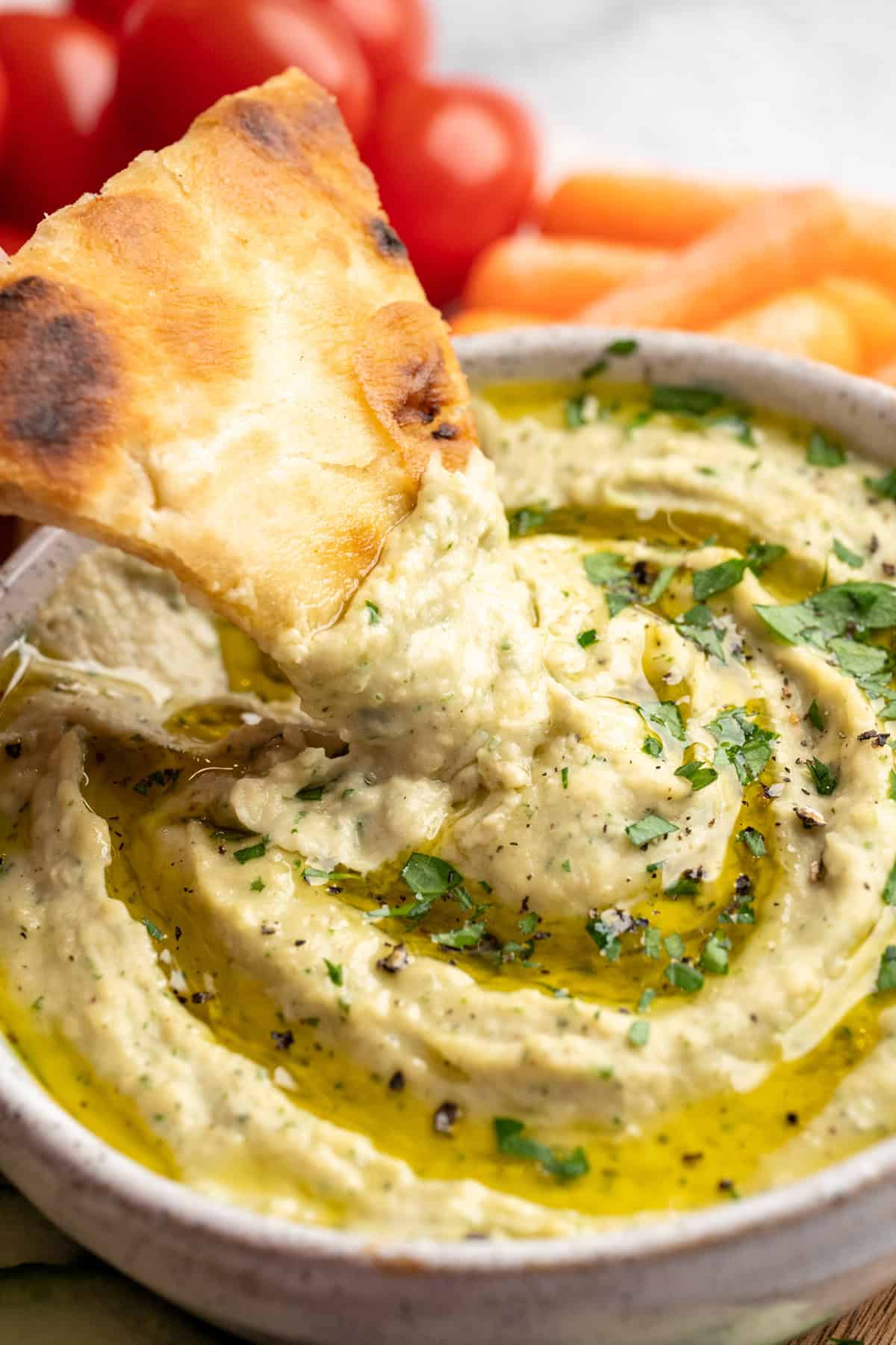 Pita chip in bowl of roasted garlic white bean dip.