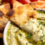 Pita chip dipping into roasted garlic white bean dip.
