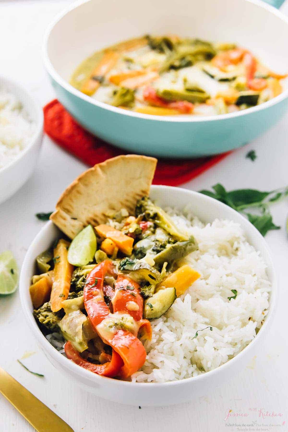 Two bowls of thai green curry with rice on the side. 