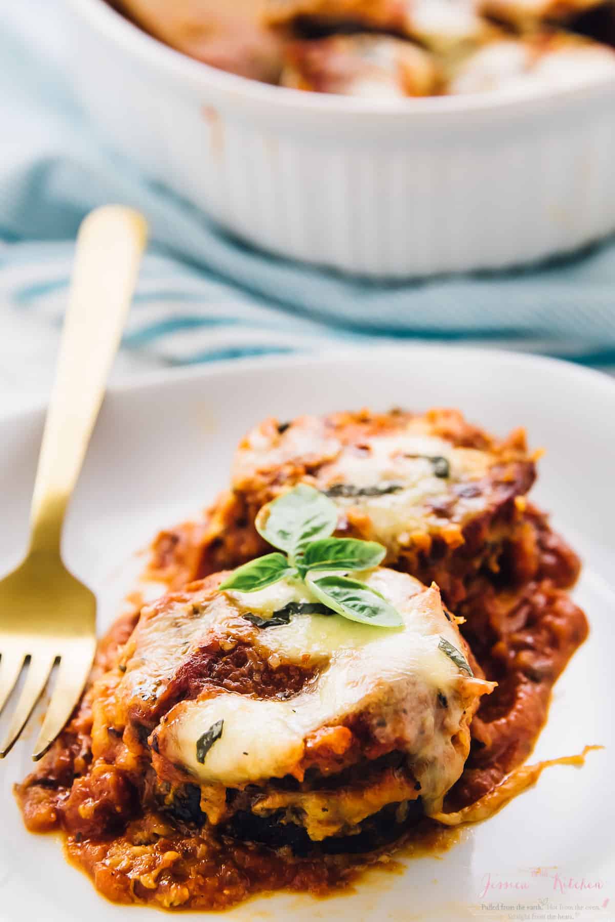 Eggplant parmesan on a white dish with a gold fork on the side. 