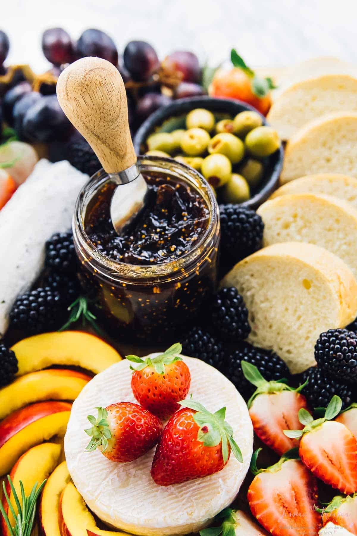 A board with jam, fruit and bread. 