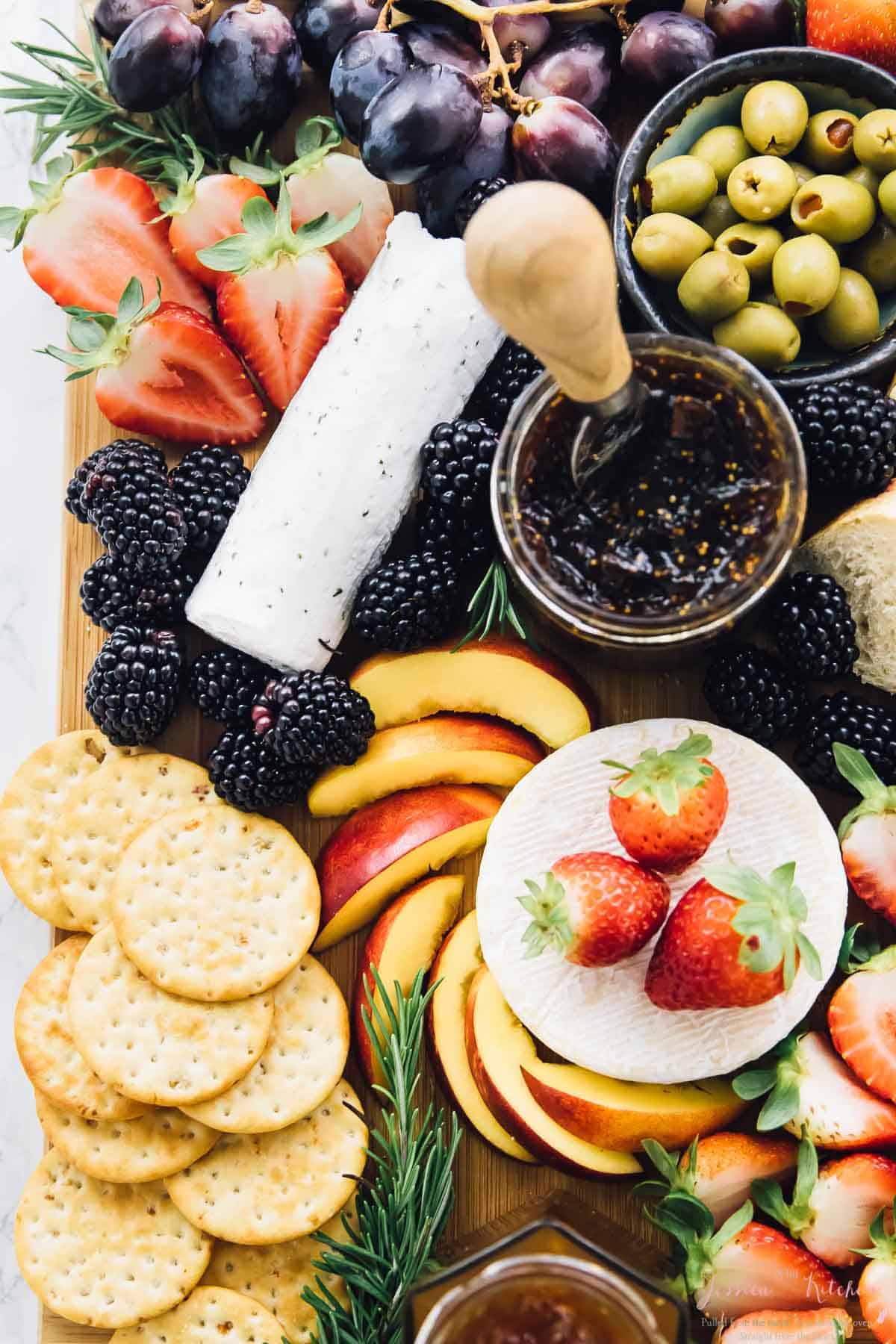Overhead shot of wood board with cheese, fruit, jam and olives on it. 