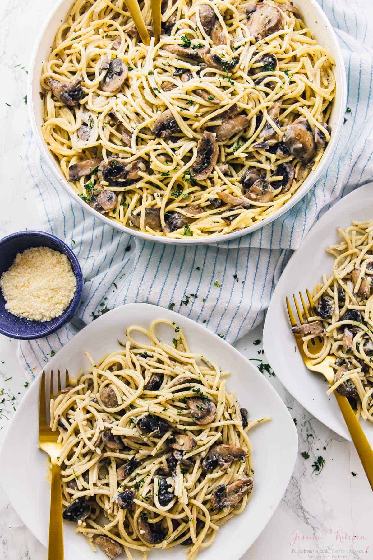 Overhead shot of creamy garlic mushroom pasta in a big bowl and on some plates. 