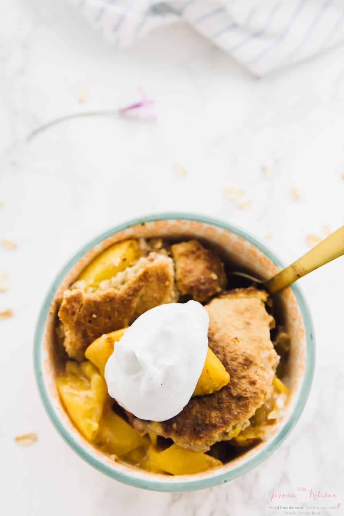 Overhead view of breakfast peach cobbler in bowl with dollop of coconut cream