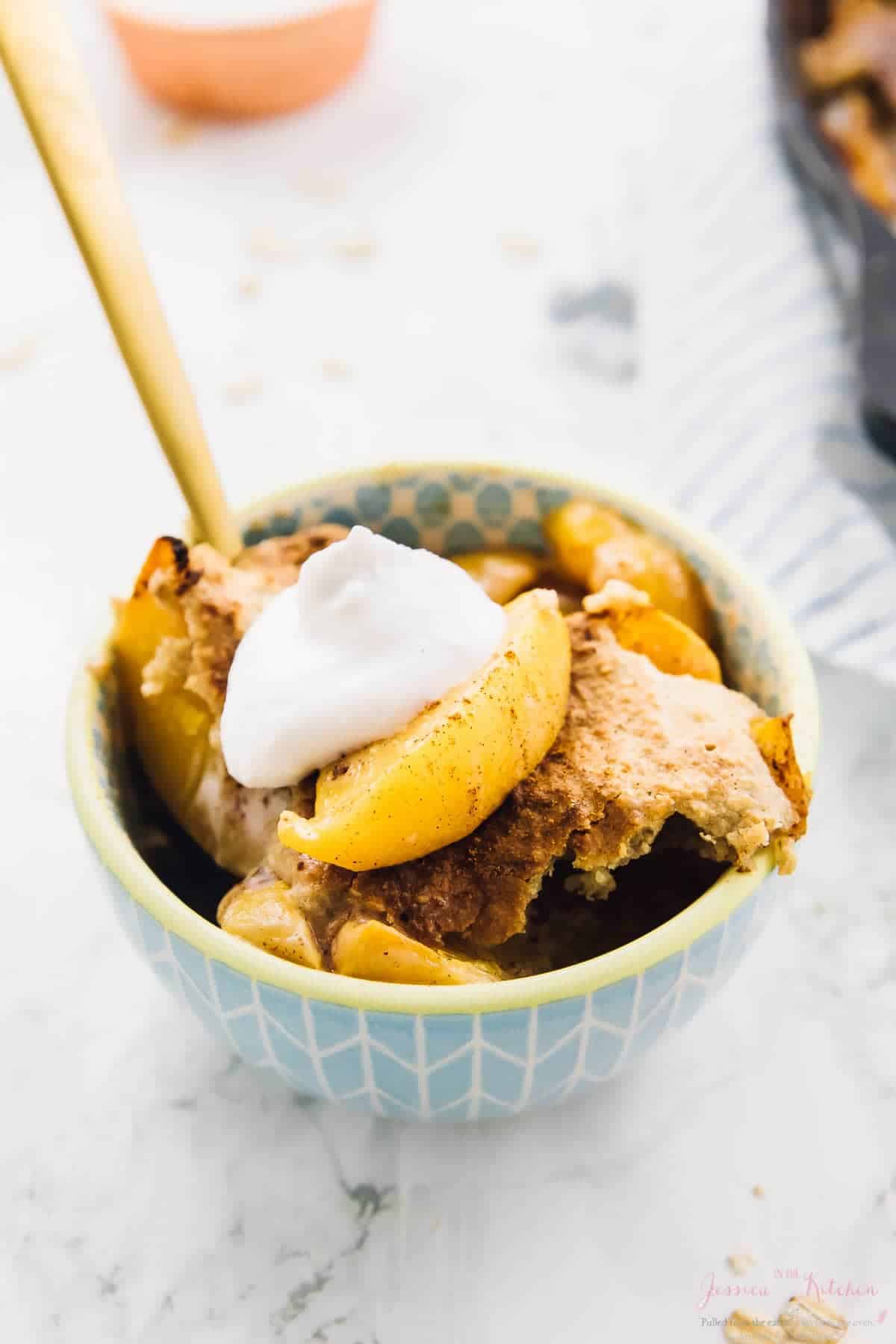 Peach cobbler in blue bowl with a gold spoon in it. 