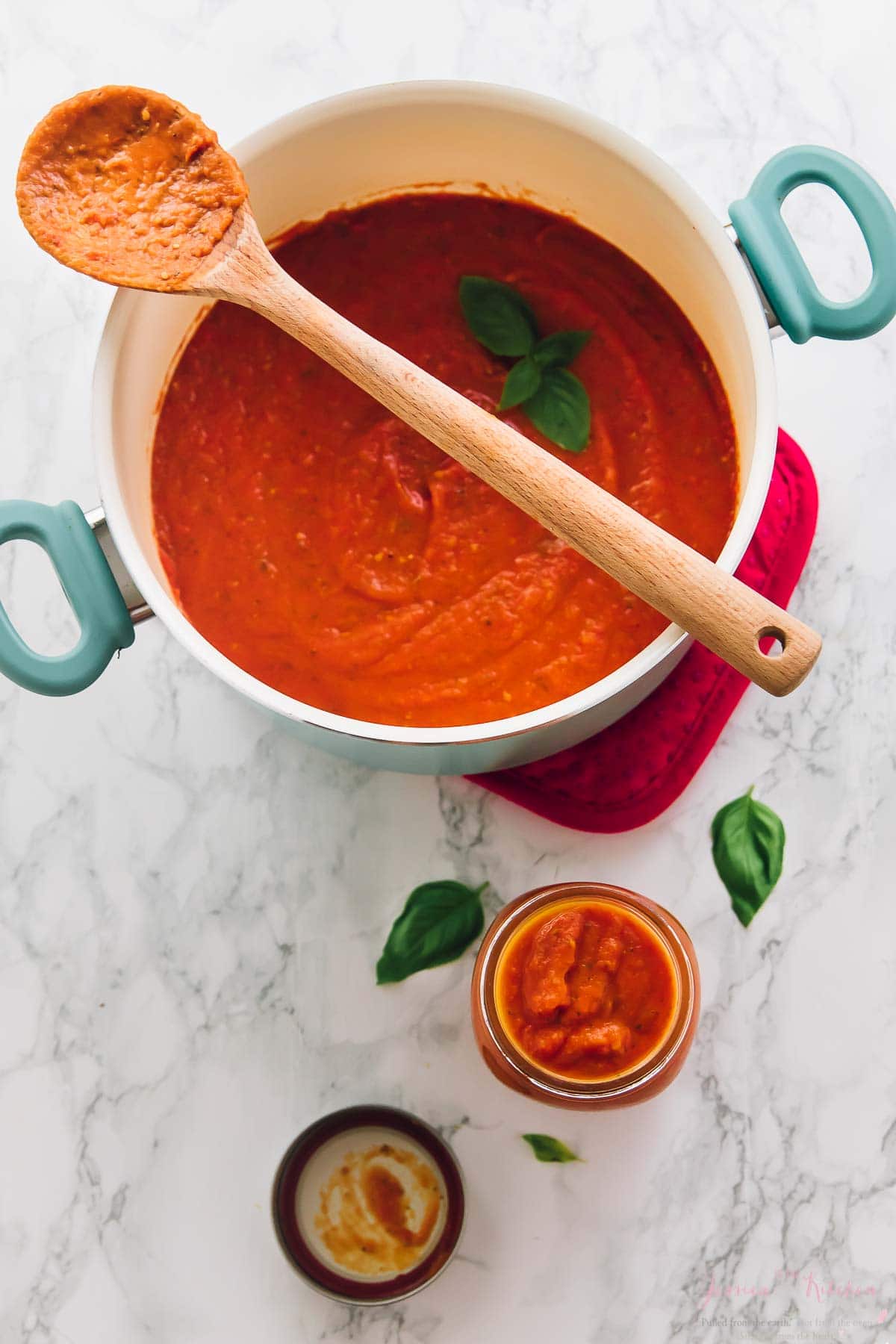 Overhead shot of roasted garlic tomato sauce in a blue pot with a wooden spoon on top.