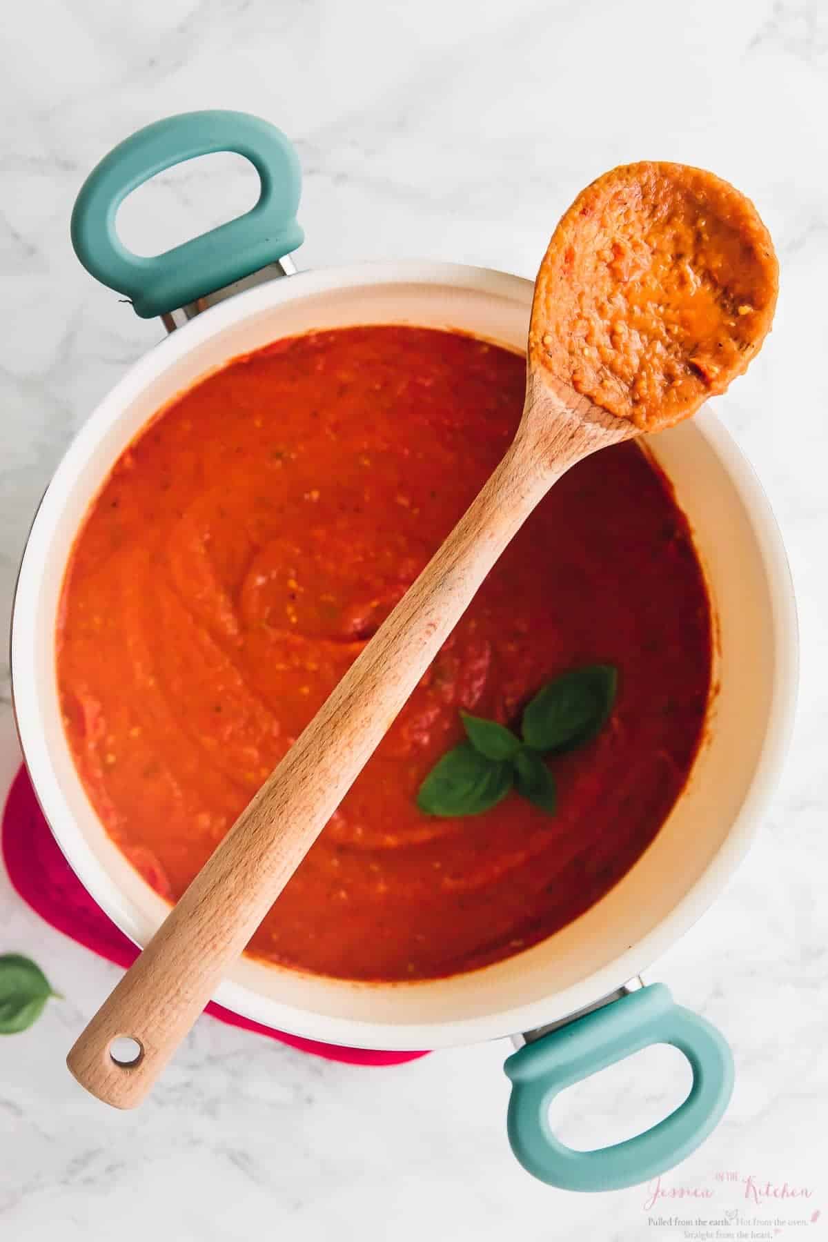 Overhead shot of tomato sauce in a pot with a wood spoon on top. 