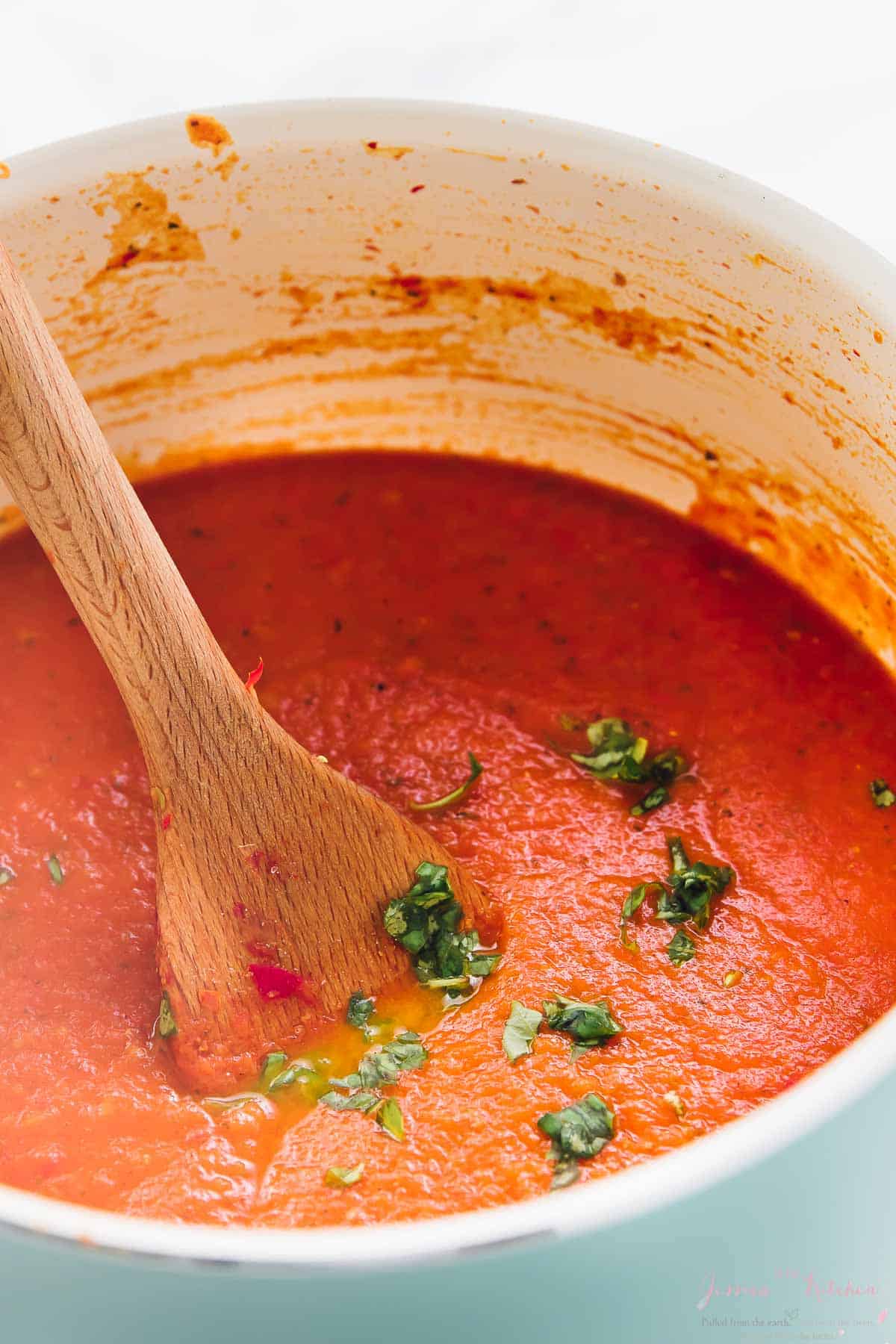 A wood spoon stir a pot of tomato sauce. 