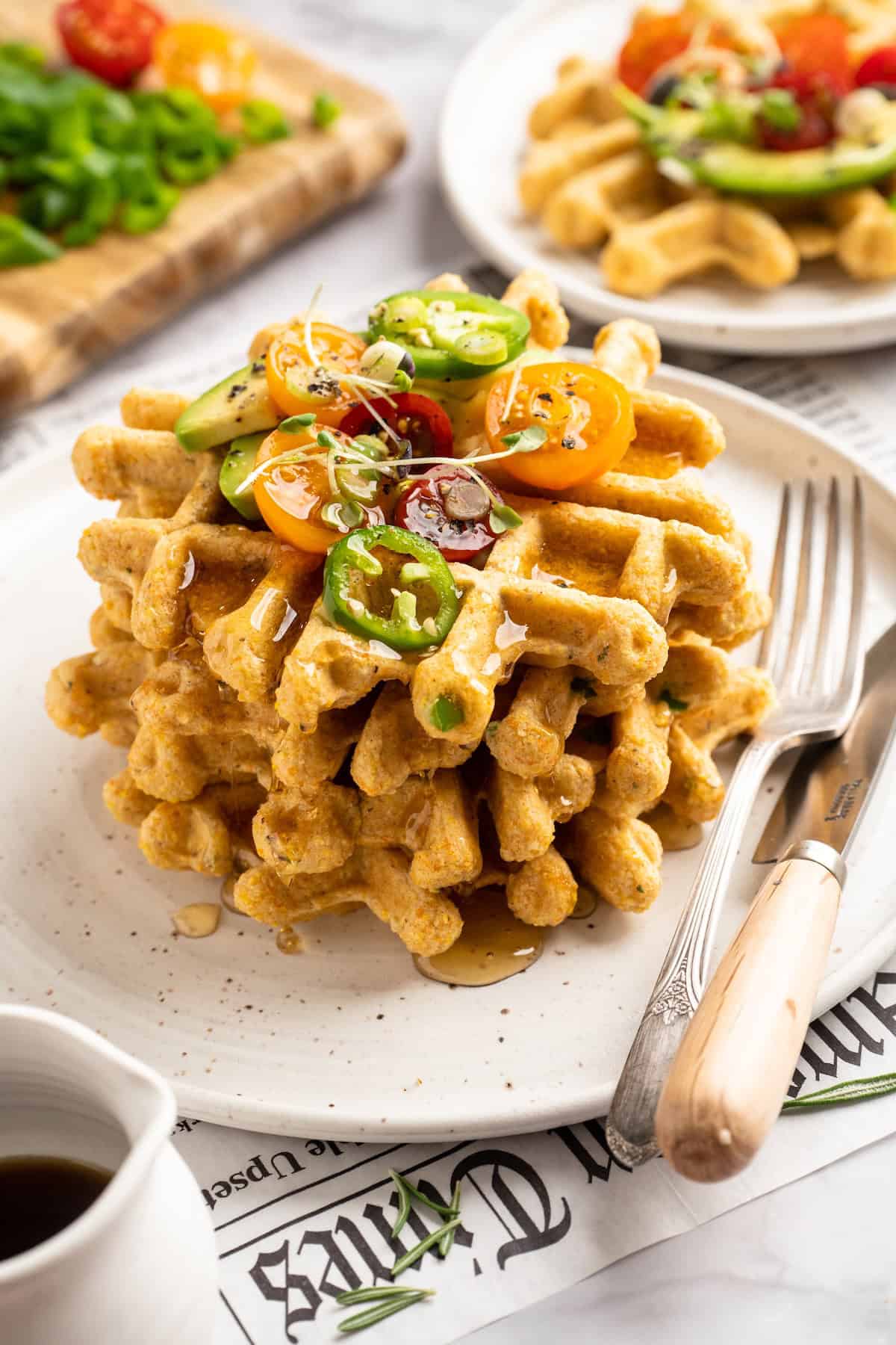 Stack of 3 cornbread waffles on plate topped with tomatoes, jalapenos, and microgreens