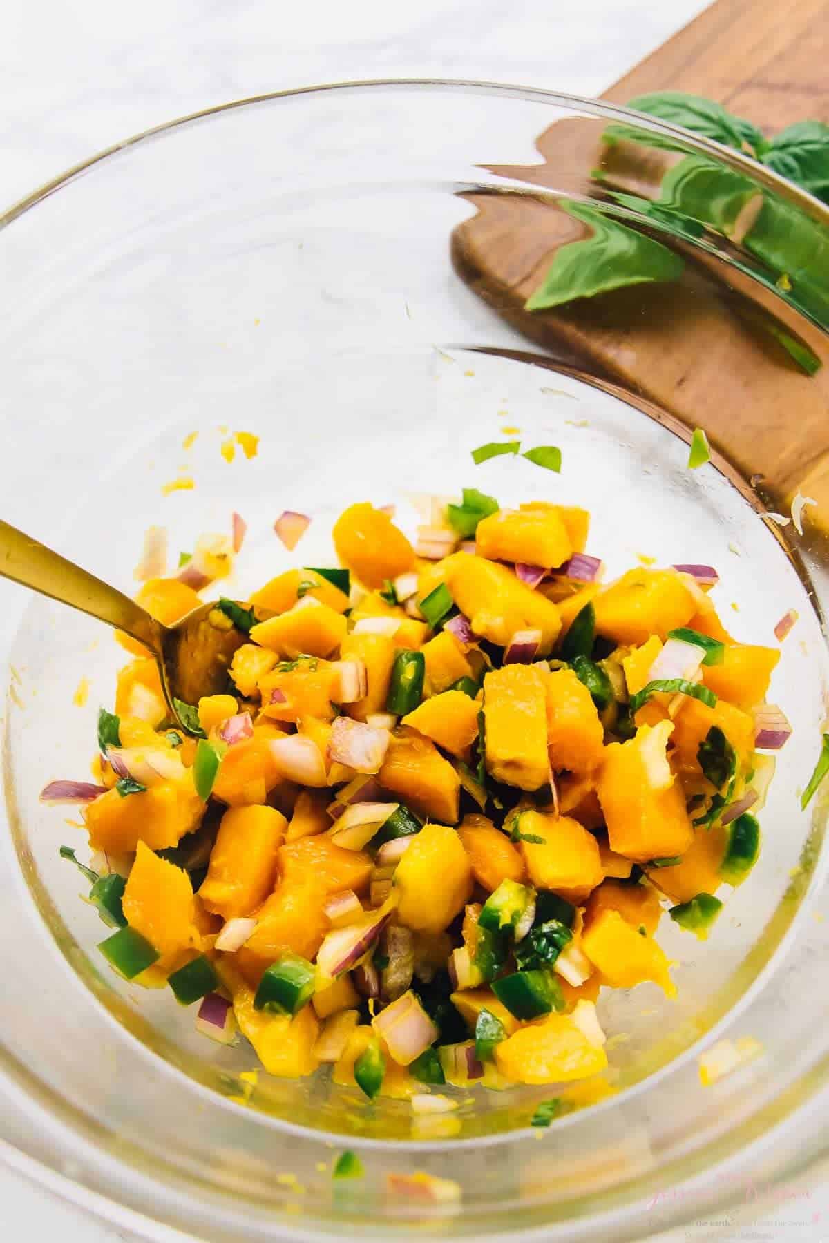Mango basil salsa with spoon in mixing bowl