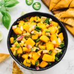 Overhead shot of mango salsa in a bowl with pita chips in background