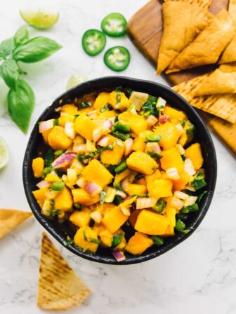 Overhead shot of mango salsa in a bowl with pita chips in background