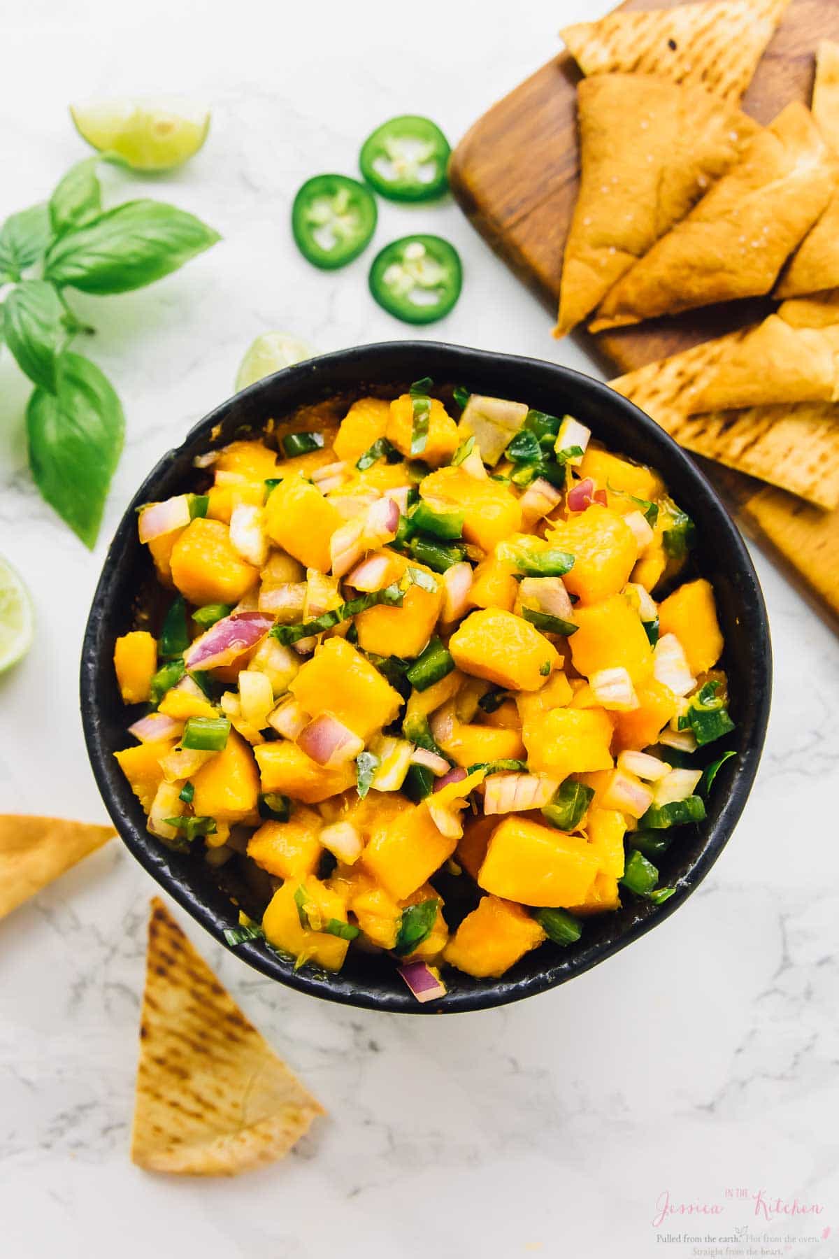 Overhead shot of mango salsa in a bowl with pita chips in background