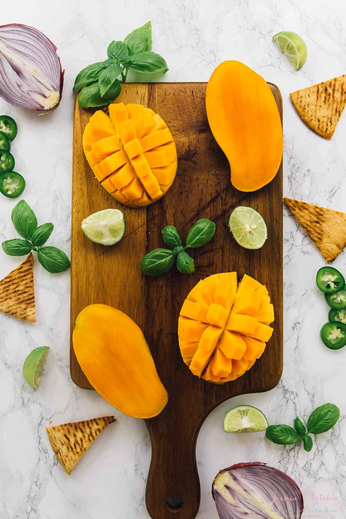 Overhead view of cut mangoes on wood cutting board with basil and limes