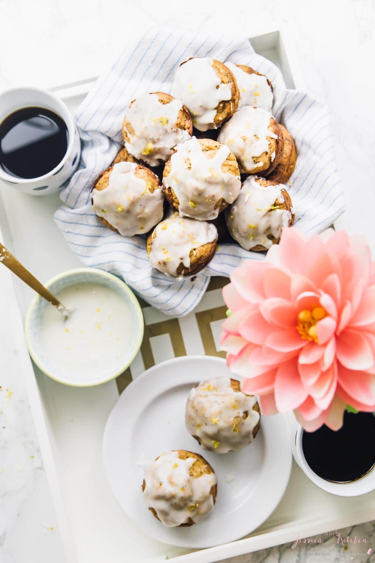 Top down shot of lemon poppyseed muffins on a serving tray with a mug of coffee and a flower. 